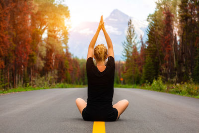 Rear view of woman with arms raised sitting on road