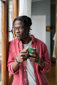 Depressed sad african guy holding cup of tea looking out window, having problems in personal life