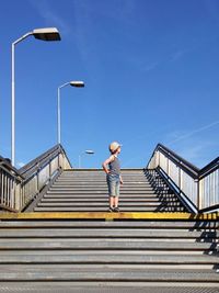 Boy standing on steps against blue sky