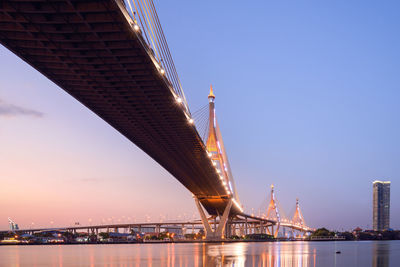 Low angle view of illuminated bridge over river in city against sky at dusk