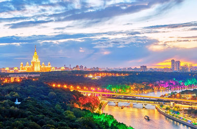 Sunset panorama of river with illuminated bridge, tourist boats and moscow university on horison