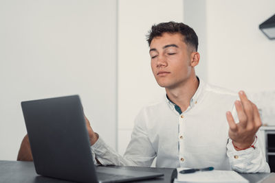 Portrait of young man using laptop at desk in office