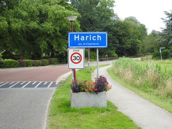 Road sign by trees against sky