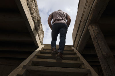 Rear view of adult man climbing up the wooden stairs, indoor toward the rooftop