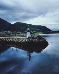 Lighthouse amidst buildings and mountains against sky