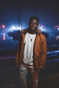 Portrait of young man standing at harbor in night