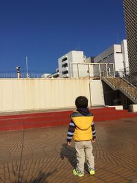 Rear view full length of boy standing against building