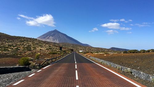 Road leading towards mountains against blue sky