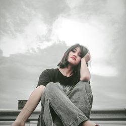 Portrait of beautiful young woman sitting against sky