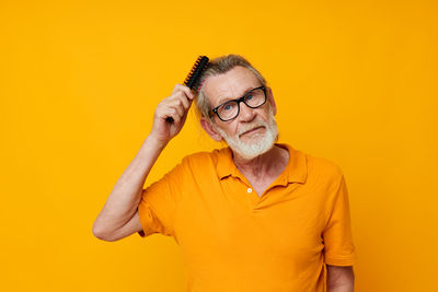 Portrait of man combing hair against yellow background