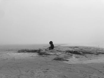 Rear view of man walking at beach against clear sky