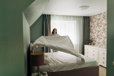 A woman makes her bed with a blanket in the morning. the woman does housework and cleaning.