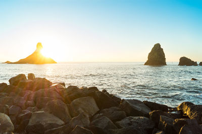 Rocks on beach against sky during sunset