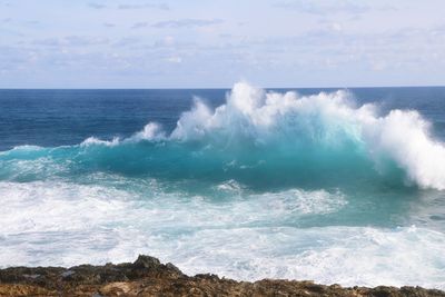 Wave splashing at sea shore against sky