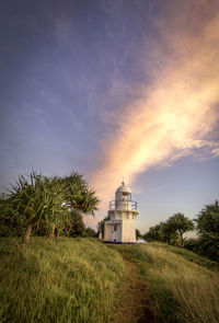 Lighthouse on field against sky at sunset