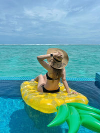 Rear view of woman in swimming pool in sea against sky