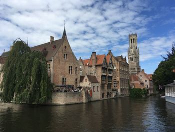 View of buildings by river against cloudy sky