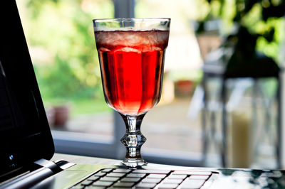 Close-up of red drink in glass by laptop on table 