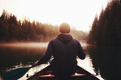 Rear view of man in boat on lake against trees