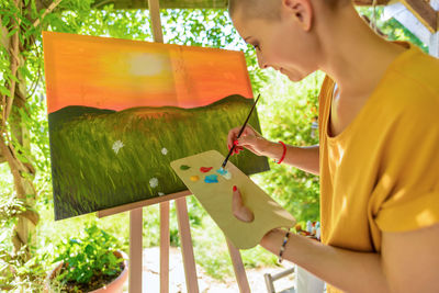 Young female artist working on her art canvas painting outdoors in her garden. 