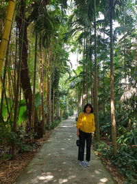 Full length of smiling mature woman standing on footpath amidst trees