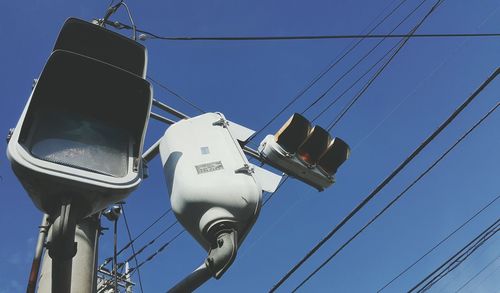 Low angle view of traffic light and power lines against clear blue sky