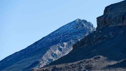 Low angle view of snowcapped mountains against clear blue sky