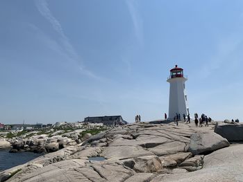 Lighthouse by sea and buildings against sky