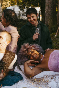 Smiling transwoman lying down by lgbtq friends during dinner party in back yard