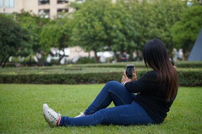 Woman photographing while sitting on grass in park