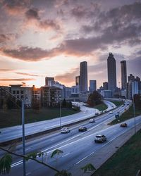 Vehicles on road in city against sky during sunset