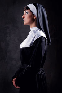 Side view of nun standing against black background