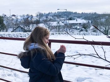 Side view of cute girl standing by fence on snow covered field during winter