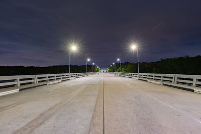 Illuminated street light on footbridge against sky at night