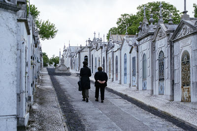 Rear view of woman walking on road amidst tombstones in cemetery