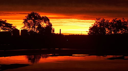 Silhouette trees by lake against romantic sky at sunset