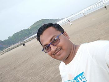 Portrait of smiling young man standing on beach against sky