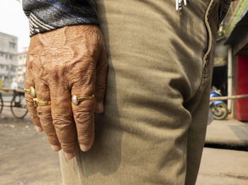 The palm of a person's right hand with a ring on his finger hangs straight at his feet