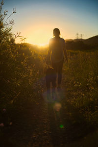 Rear view of woman walking on field with dog against sky during sunset