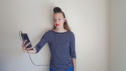 Teenage girl listening to music while using phone against wall