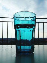 Close-up of water in glass on table against sky