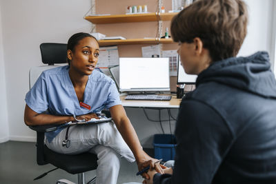 Female medical professional consoling teenage patient while sitting in examination room at clinic