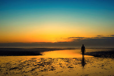 Rear view of silhouette man walking on beach at sunset