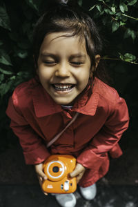 Cute little girl smiling and holding an instax orange camera.