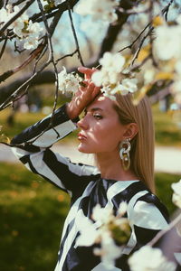 Side view of thoughtful young woman standing below white cherry blossoms