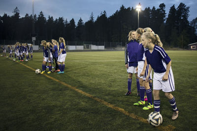 Girls standing with soccer balls on field