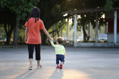 Rear view of mother holding son hand while walking on footpath