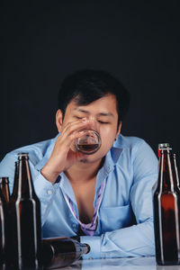 Portrait of mid adult man holding bottle against black background