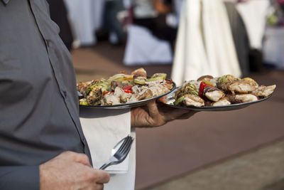 Midsection of waiter holding food in plate 