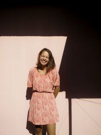 Young woman laughing while standing by wall at home